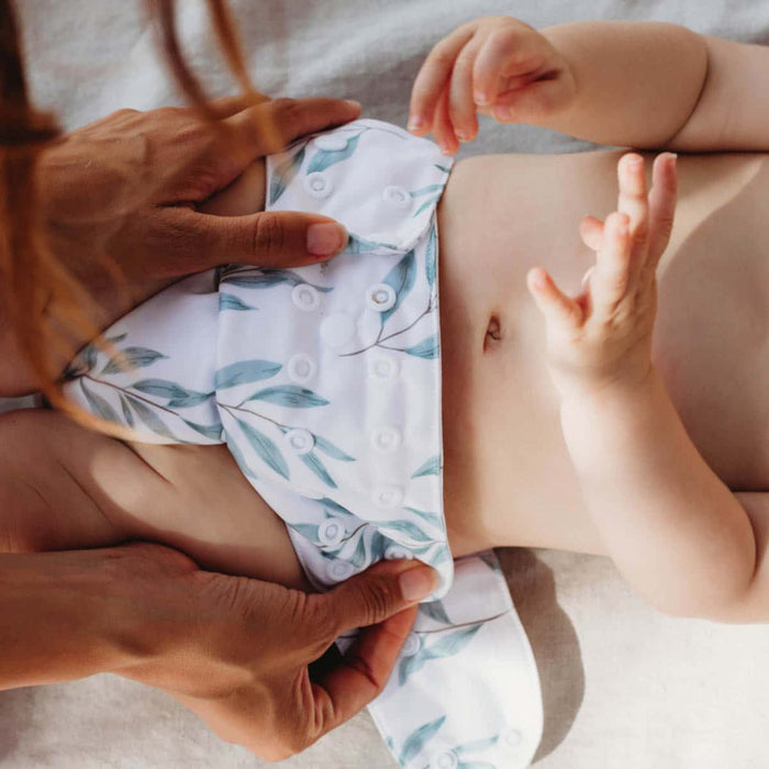 Mum adjusting snaps of cloth nappy on her baby.