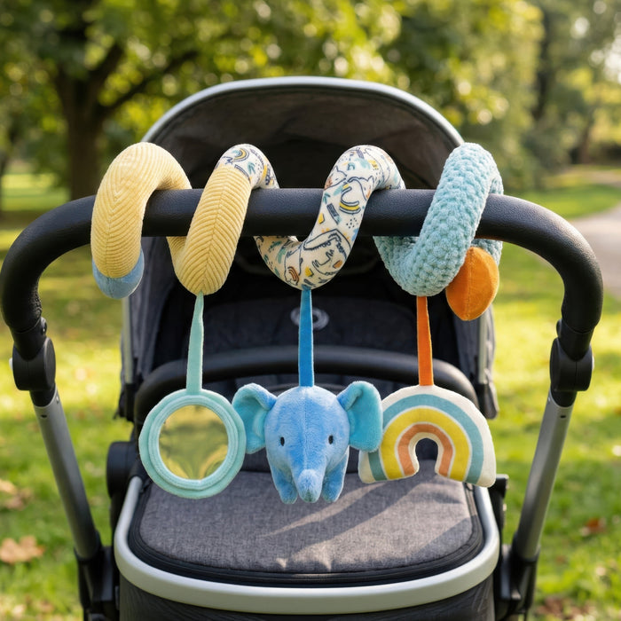 The Animal Adventures Spiral Activity Toy | Elephant decorates a stroller handle with a mirror, blue elephant, and rainbow for sensory fun. Shown outdoors in a sunny, green park, this toy encourages developmental play for little ones.