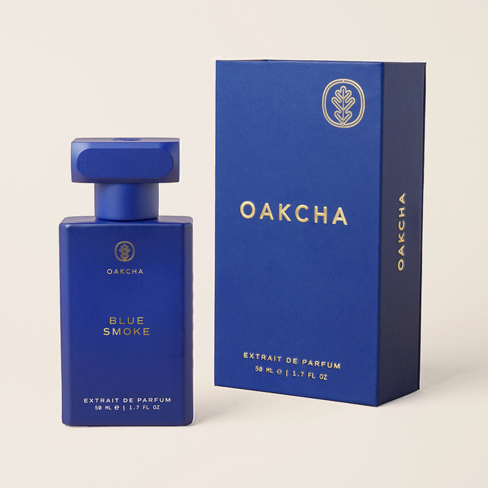 Angled view of Blue Smoke perfume bottle and box showing matte cobalt-blue glass with gold Oakcha logo on neutral background
