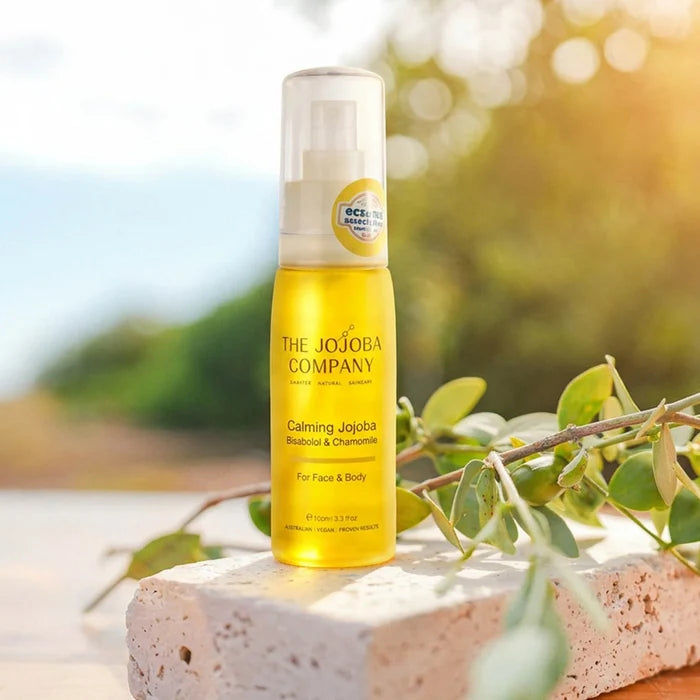Bottle of yellow The Jojoba Company Calming Jojoba on a natural background with greenery.