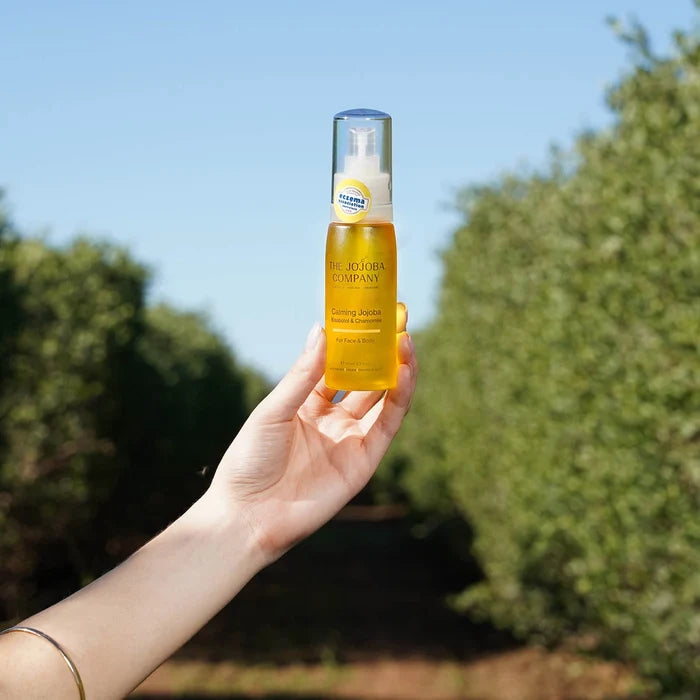 Hand holding a bottle of calming jojoba with a blurred natural background