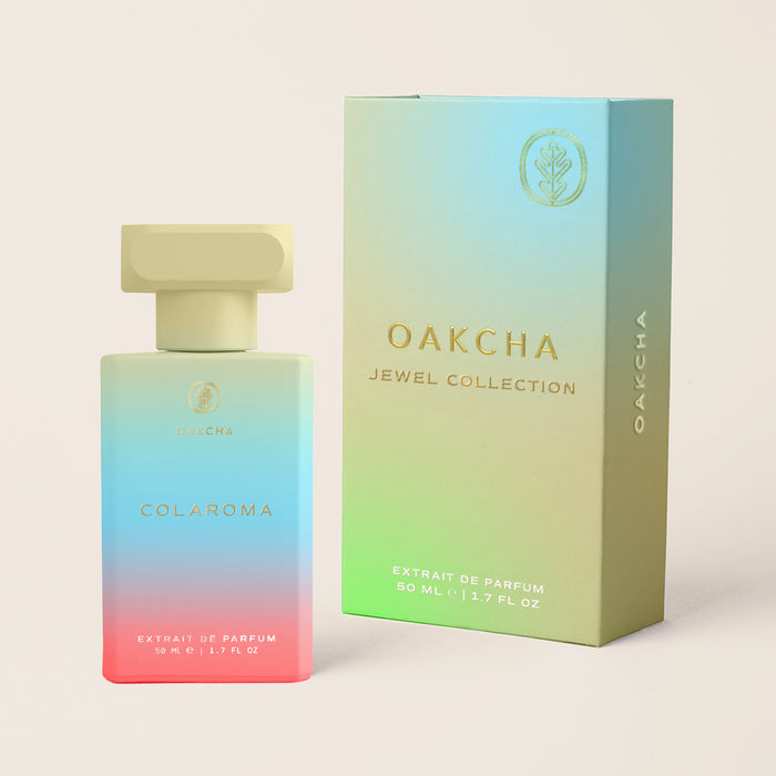 Front view of Colaroma perfume bottle and matching gradient box showing ombre pastel glass and gold cap on beige background
