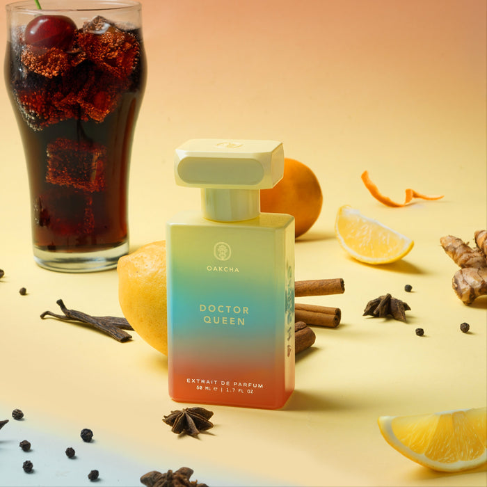 Front view of Dr. Queen perfume bottle with gradient blue-to-coral glass and cap on beige backdrop with orange slices