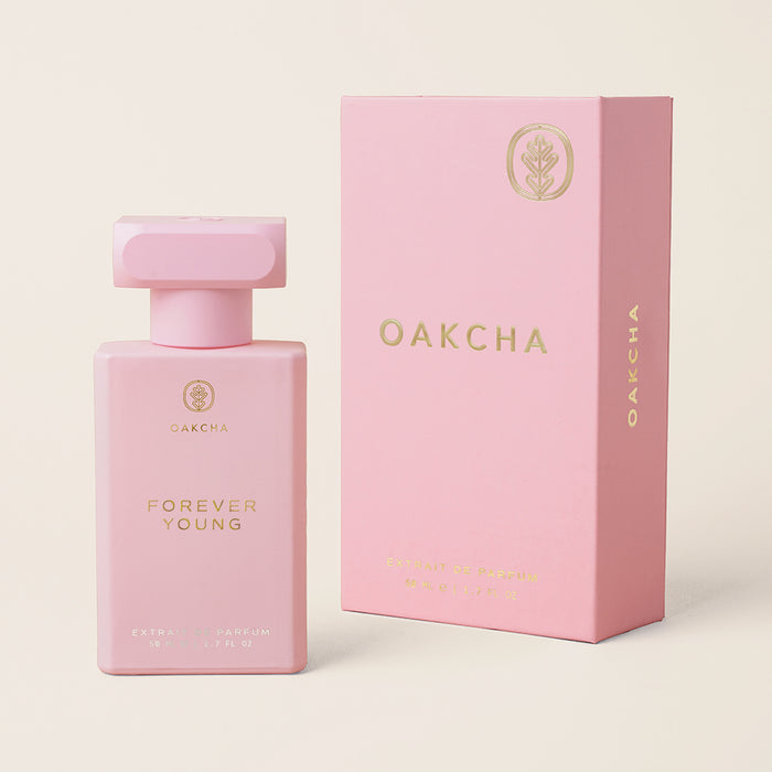 Front view of Forever Young perfume bottle and matching pink gift box showing gold logo on a light beige background