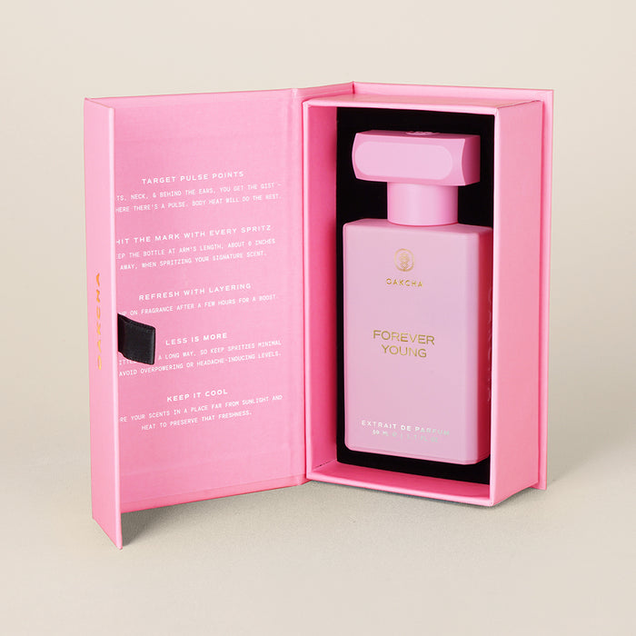 Front view of Forever Young perfume in open pink box, showing rectangular pink bottle with gold logo on beige background