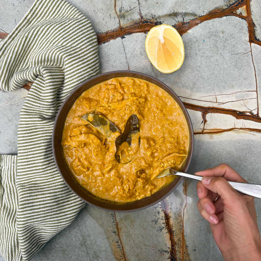 Creamy curry with bay leaves, lemon wedge, and striped napkin on marble surface
