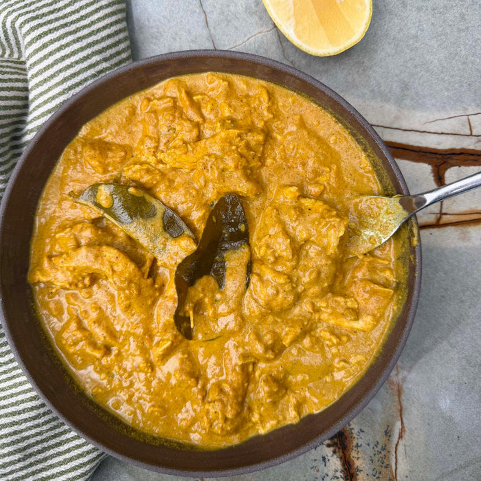 Creamy curry with bay leaves in a rustic bowl, served with lemon wedge