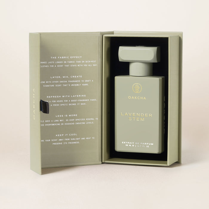 Front view of Lavender Stem parfum bottle in open sage-green gift box showcasing gold logo and lettering with neutral beige studio background