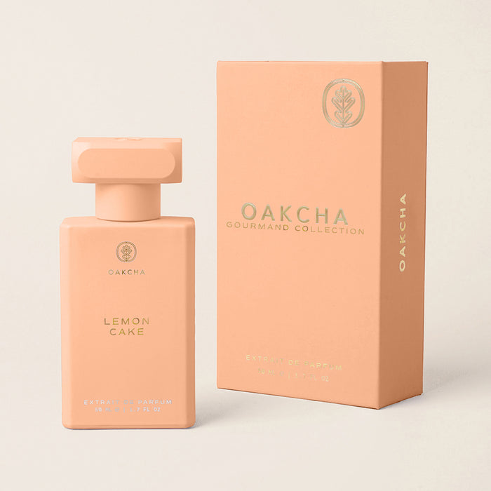 Front view of Lemon Cake perfume bottle and matching box showcasing matte peach-pink bottle with gold logo on cream background