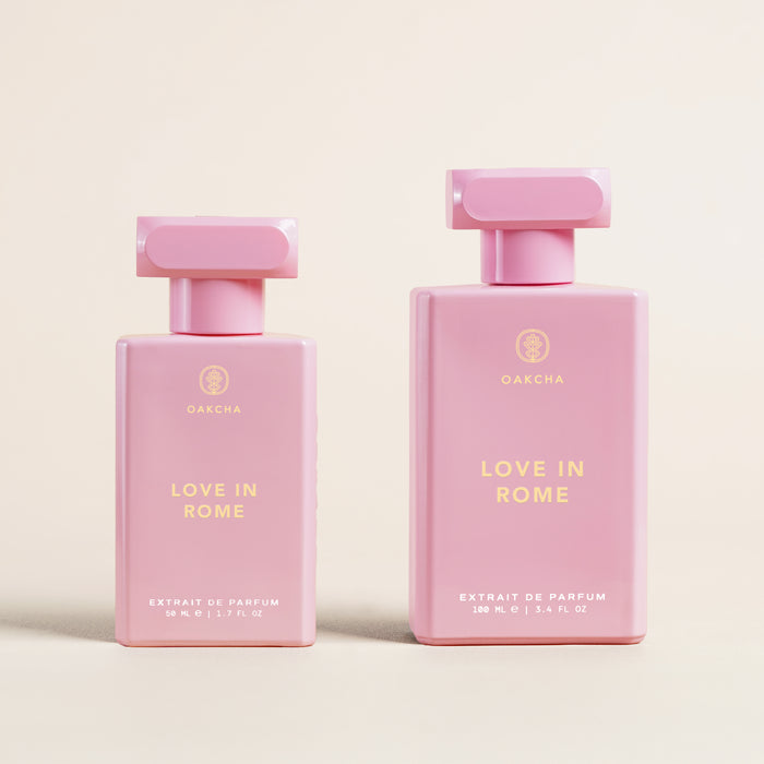 Front view of Love in Rome perfume bottles showcasing two pink rectangular bottles (50 ml and 100 ml) with gold logo on a cream background