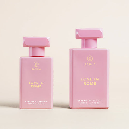 Front view of Love in Rome perfume bottles showcasing two pink rectangular bottles (50 ml and 100 ml) with gold logo on a cream background