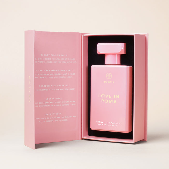 Front view of Love in Rome 100 mL perfume bottle in a pink presentation box, gold lettering and rectangular cap on a neutral backdrop