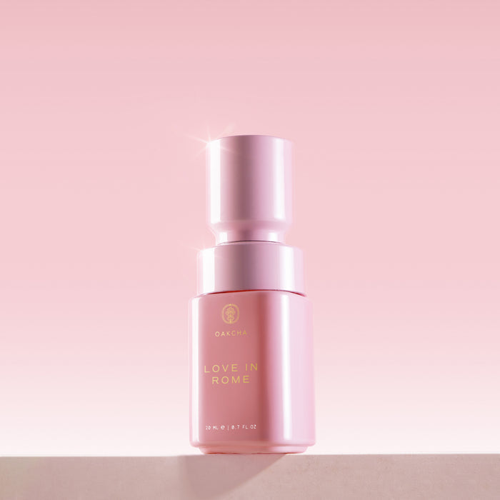Front view of Love in Rome perfume oil bottle, glossy pink cylinder with gold label and 20 mL mark on pink gradient
