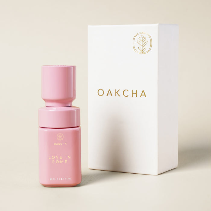 Front view of Love in Rome perfume oil bottle with matte pink finish, gold lettering and 20 ml mark next to white Oakcha box