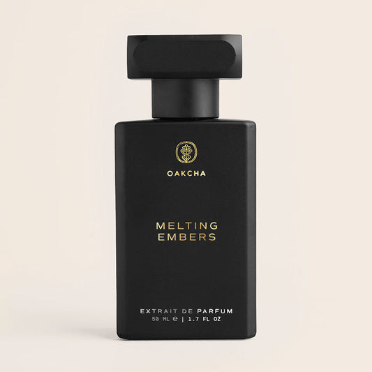 Front view of Melting Embers perfume bottle with matte black rectangular design, gold logo and text, and black cap on beige background