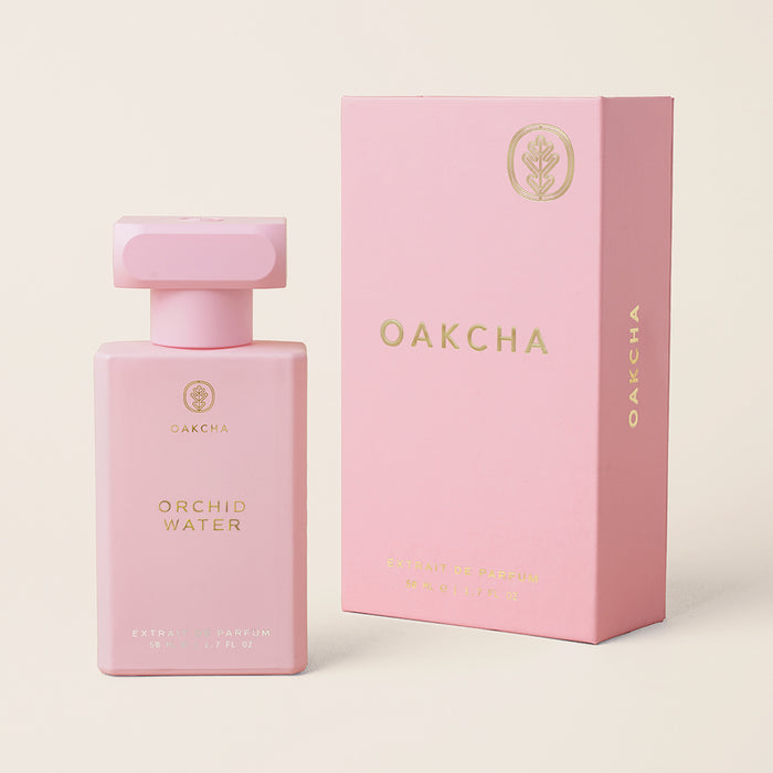 Front view of Orchid Water perfume bottle and matching pink box showcasing gold lettering on a pale pink background