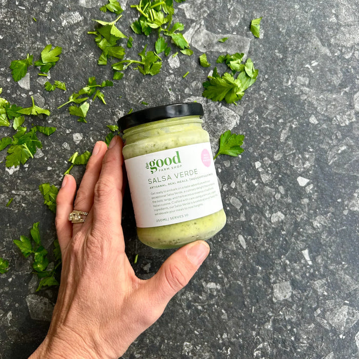 Hand holding jar of Salsa Verde with fresh parsley on stone surface, organic ready meal