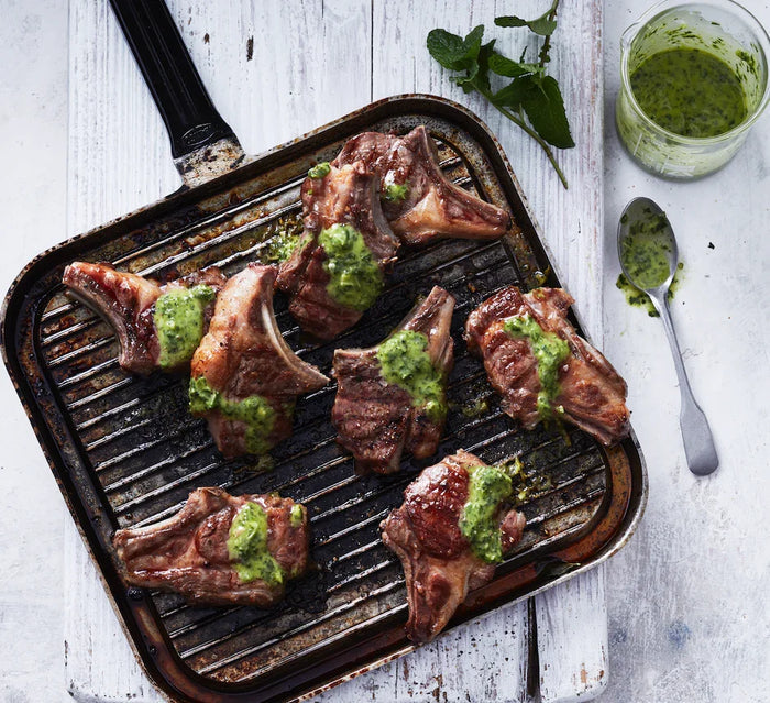 Grilled lamb chops with green herb sauce on a grill pan, fresh mint nearby