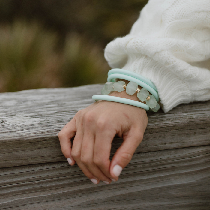 Hand wearing multiple light blue bracelets on a wooden surface