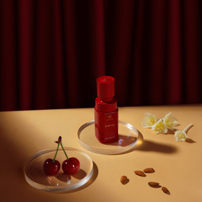 Front view of Sinful Perfume Oil 20 ml showcasing red bottle with dipstick cap on beige tabletop with cherries and almonds