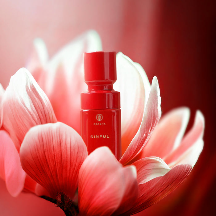 Three-quarter view of Sinful Perfume Oil bottle showcasing a red bottle and cap with a soft red floral background