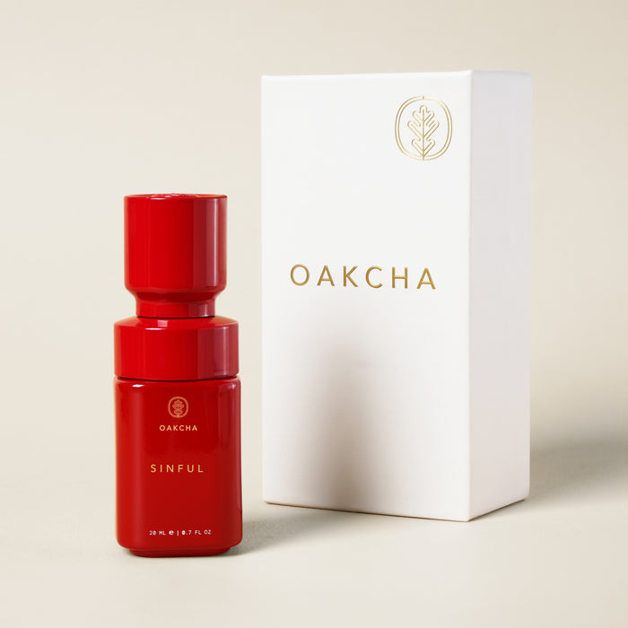 Front view of Sinful Perfume Oil red bottle showcasing glossy finish beside white Oakcha box on beige background