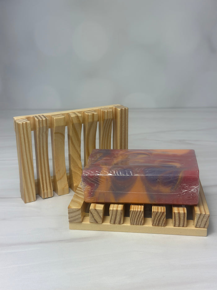 Wooden slotted soap tray with a bar of purple orange and pink sitting on it to show how it’s used
