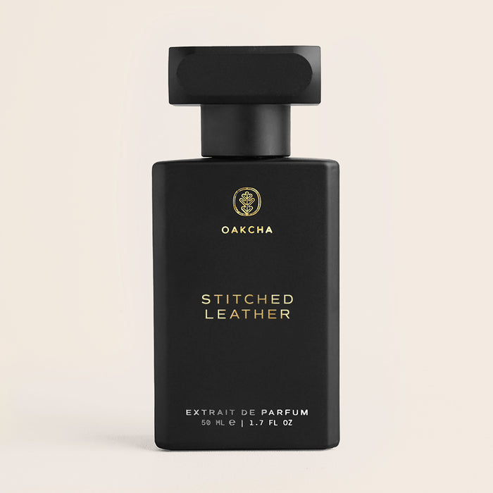 Front view of Stitched Leather perfume bottle showing black matte finish, gold logo and rectangular cap on cream background