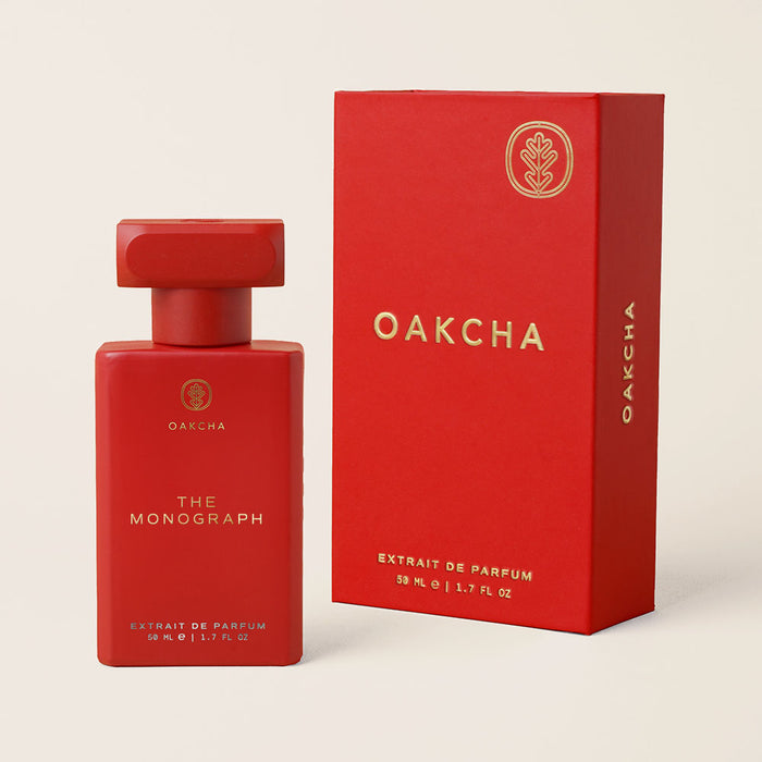 Front view of The Monograph perfume bottle and matching box in matte red with gold lettering on a beige background