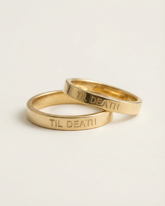 Two gold rings with 'TIL DEATH' engraving on a beige background
