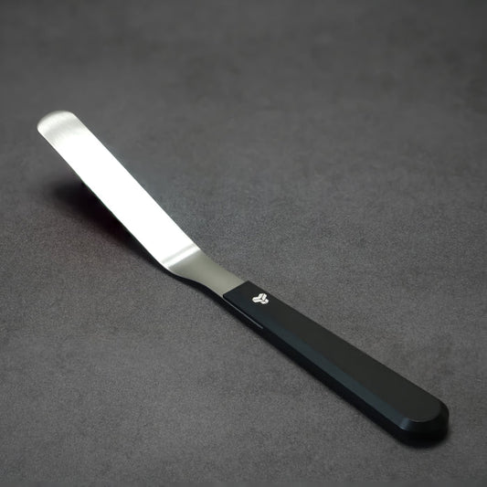 A 4 inch blade offset spatula with a black aluminum handle and a titanium blade, displayed on a dark textured surface.