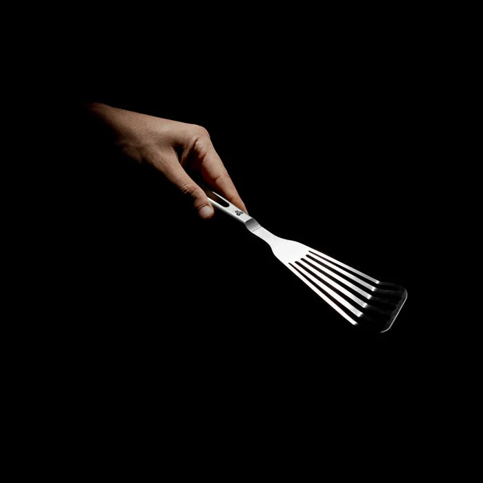 Hand holding a titanium fish turner against a black background