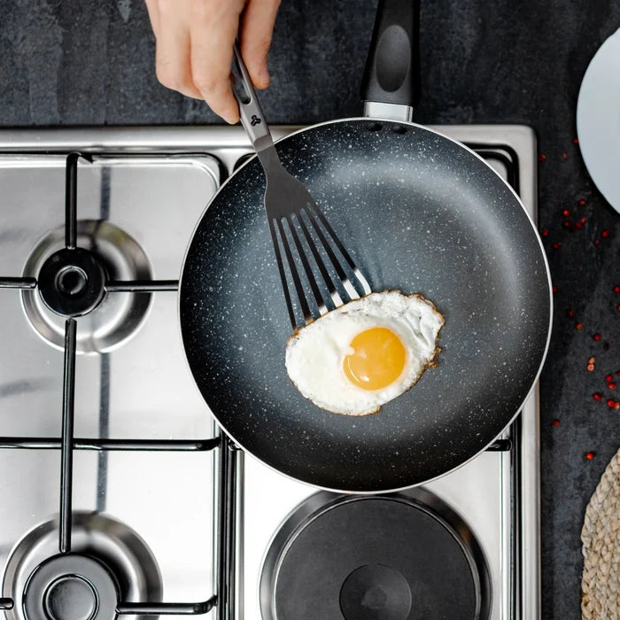 Person flipping an egg in a non-stick frying pan on a gas stove.