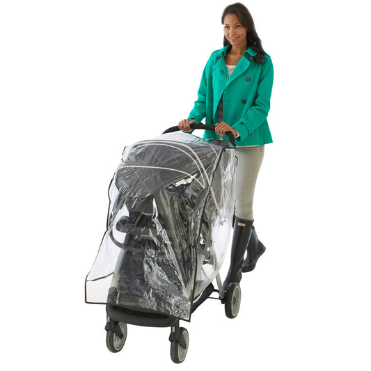 A smiling woman in a teal coat and black boots pushes a Nuby Travel System Weather Shield stroller with a clear weather cover and black frame, set against a white background.